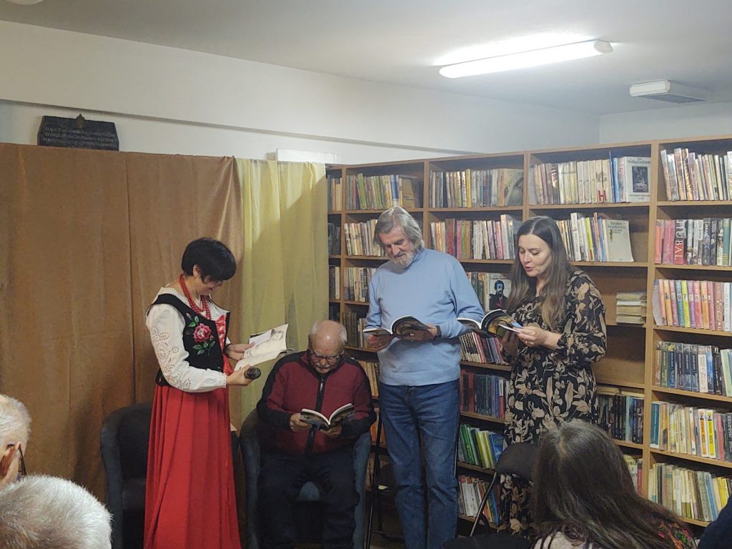 Cztery osoby na tle regałów bibliotecznych czytające scenkę z książek