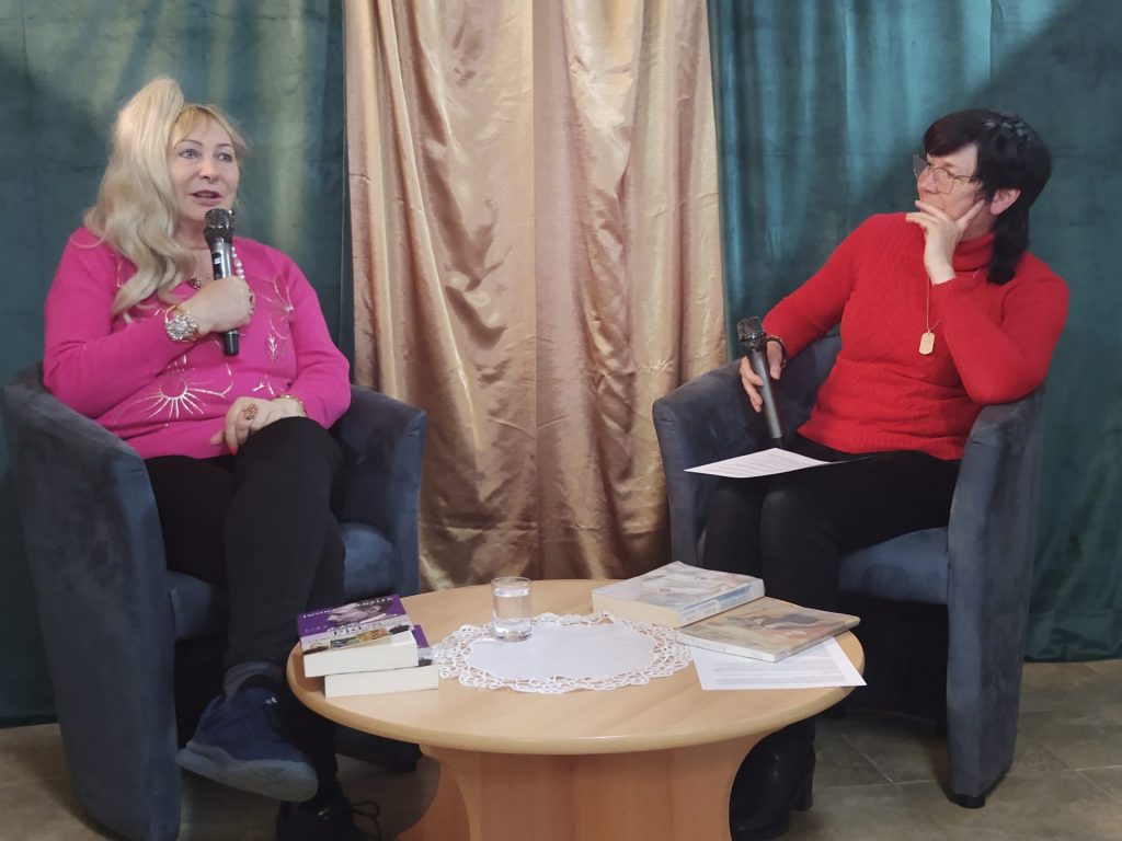 Po lewej stronie Iwona Kienzler, po prawej stronie dyrektor biblioteki, na pierwszym planie stolik z książkami